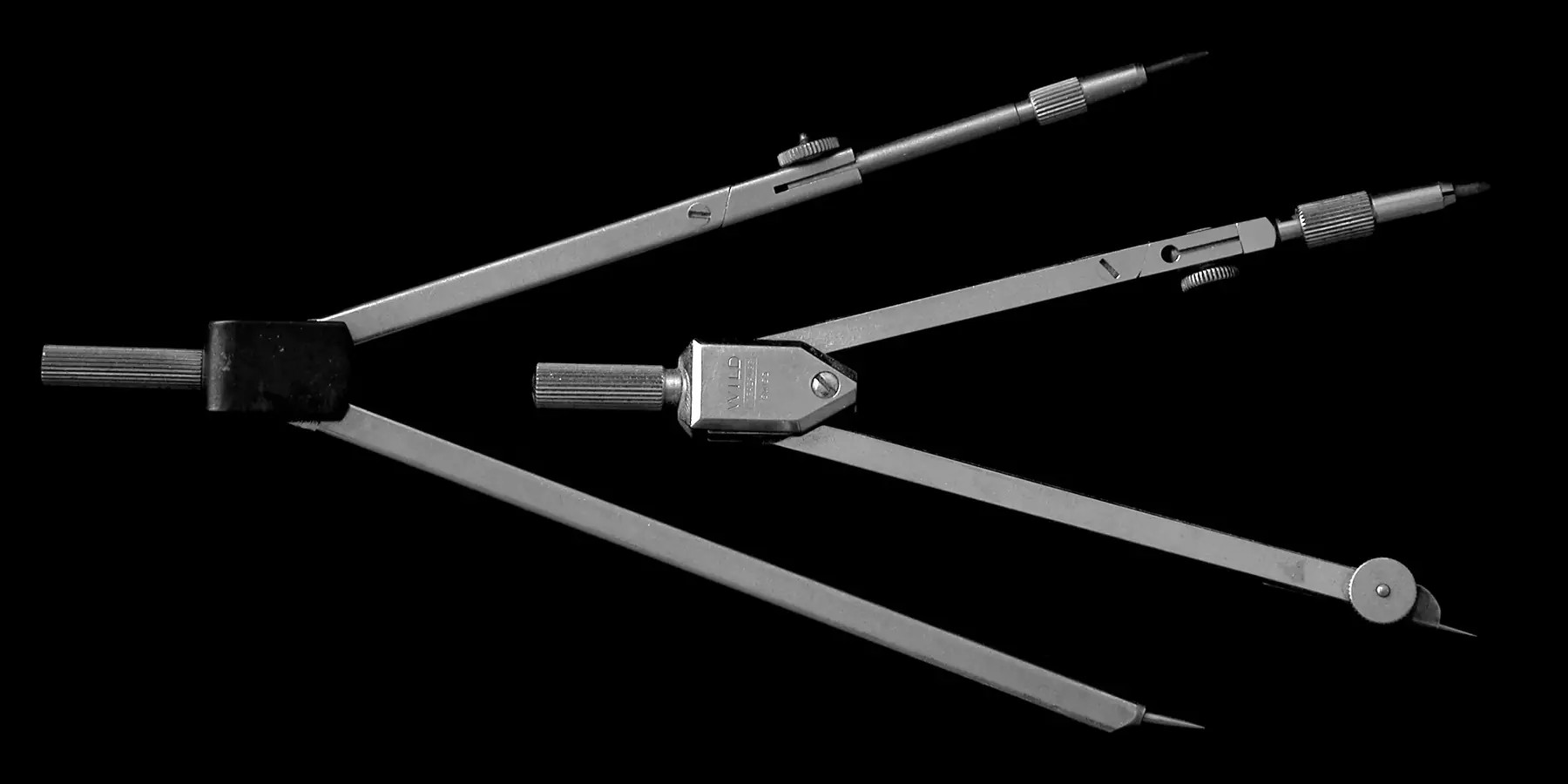 Two drafting compasses with open legs lying on a black background