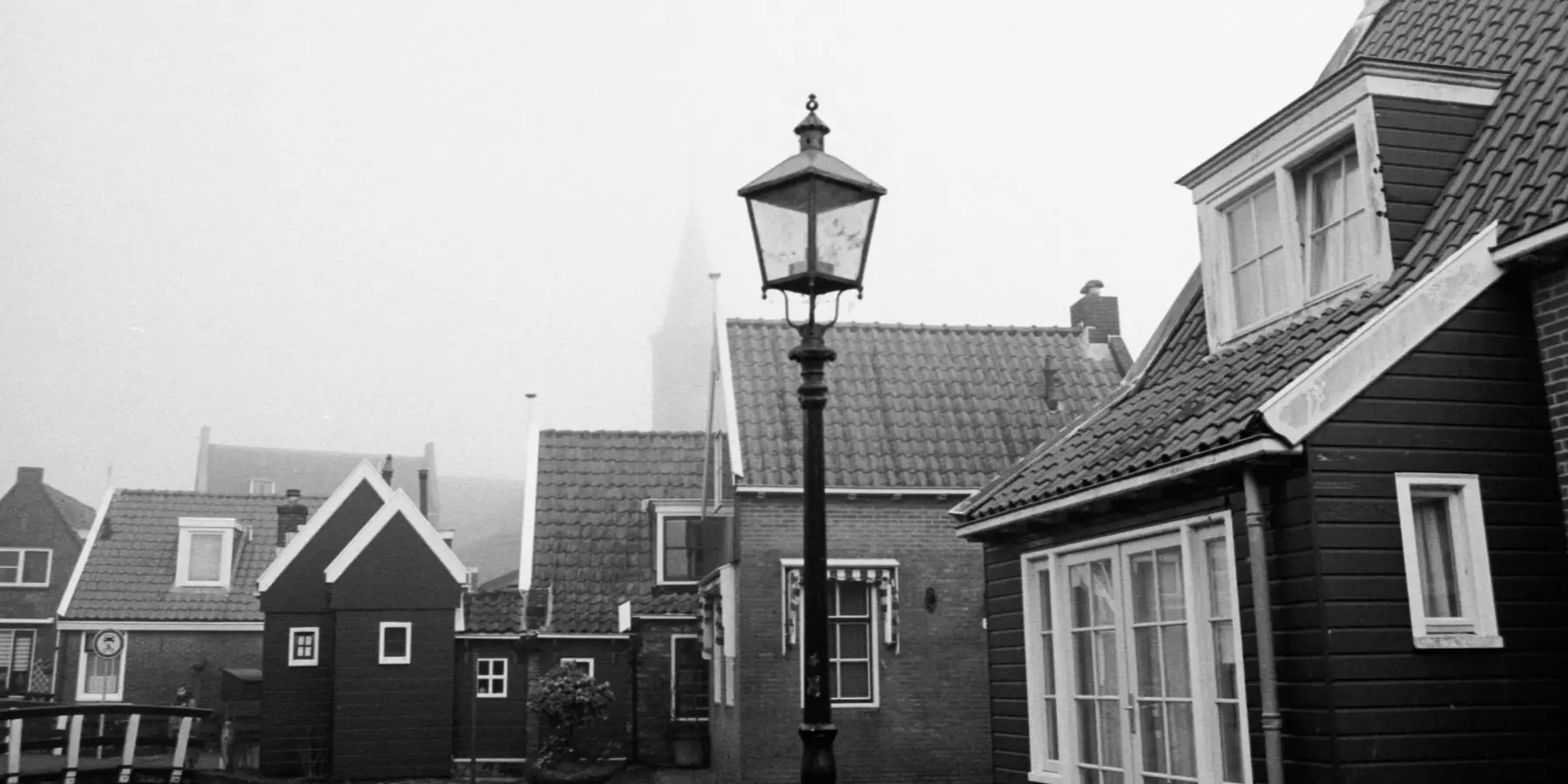 Foggy Dutch village street with dark wooden houses and a lamp post