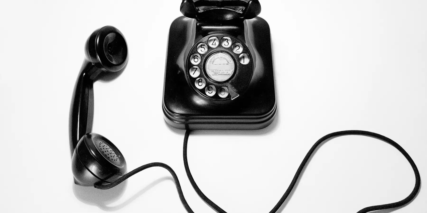 Black rotary dial telephone with its handset and cord on white