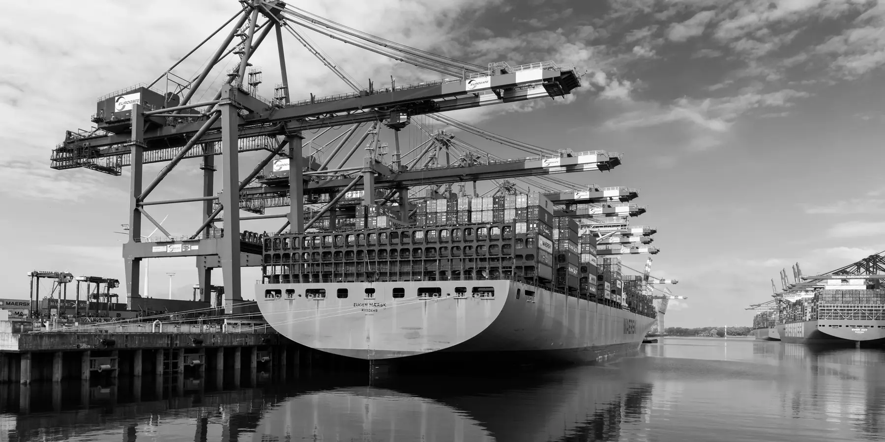 Container ship moored beneath quay cranes, reflected in still water