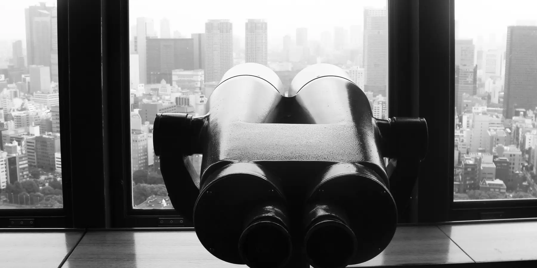 Large binoculars on a windowsill facing a hazy city skyline