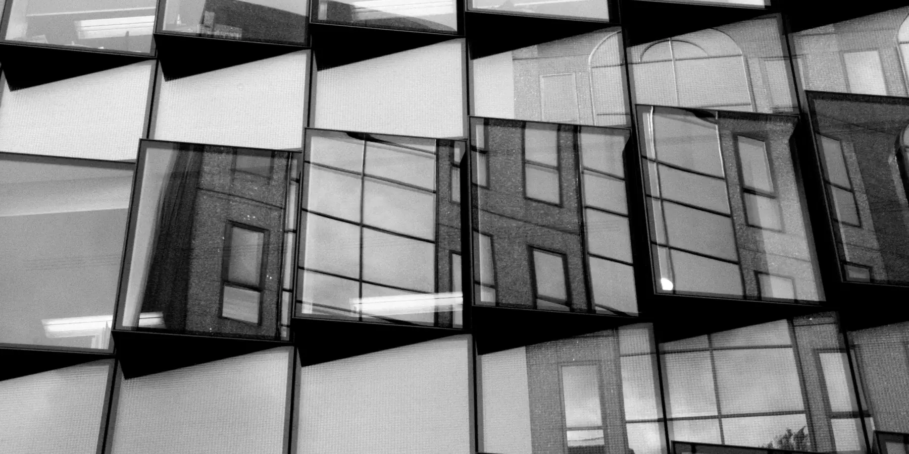 Glass facade of offset window panes reflecting neighbouring buildings
