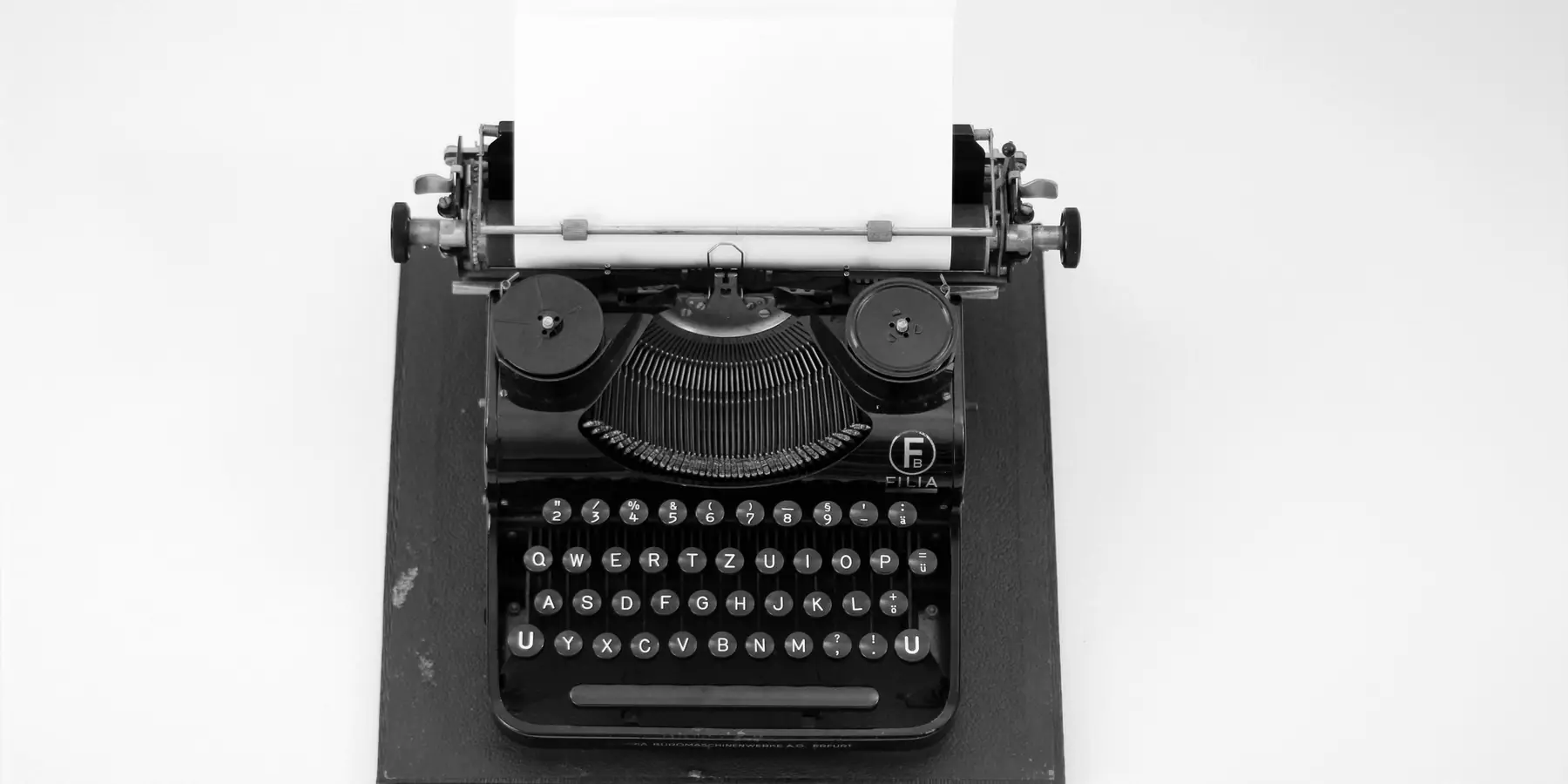 Black typewriter with a blank sheet of paper on a white table