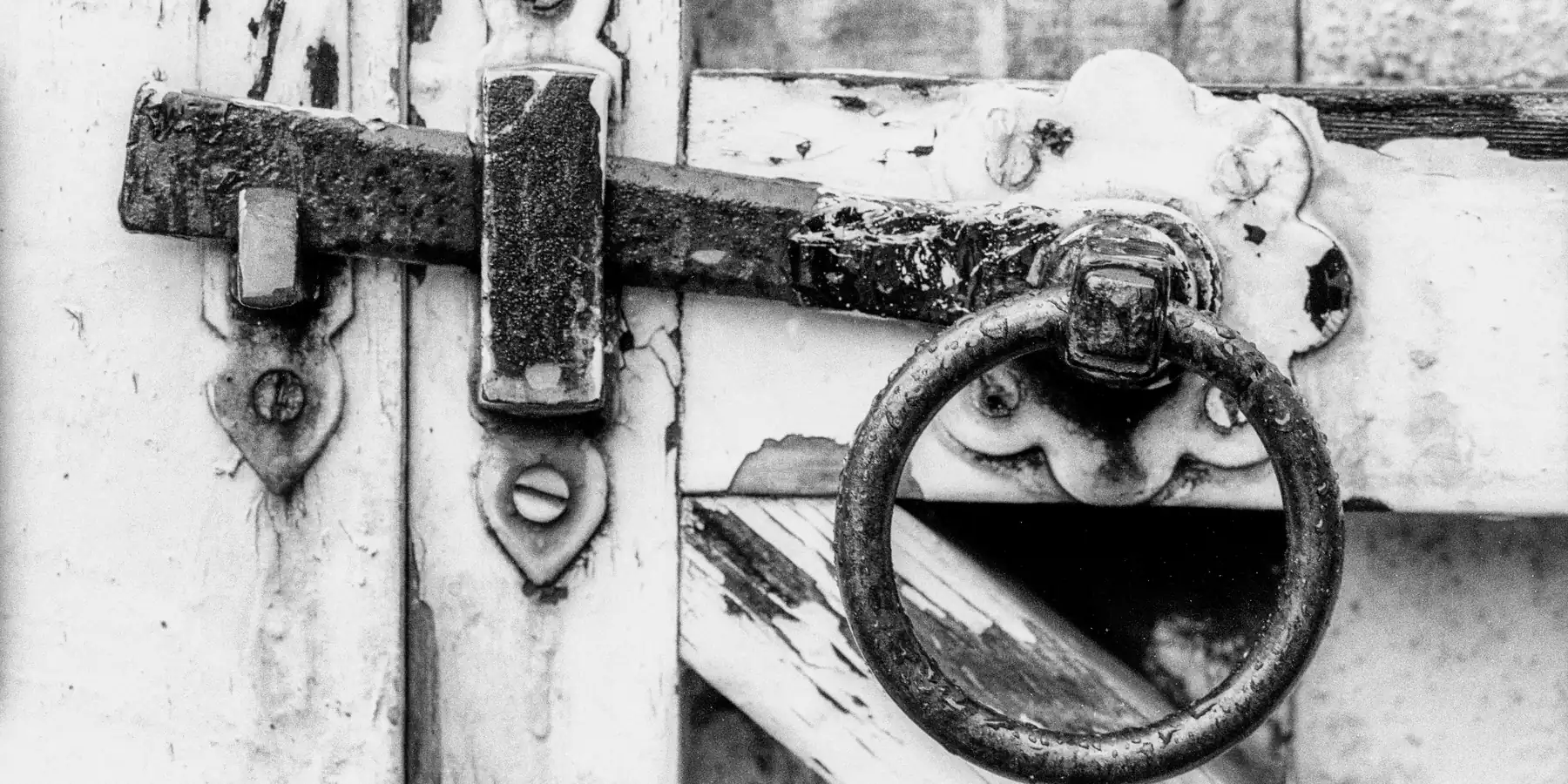 Weathered iron door latch and ring handle on a white-painted wooden gate