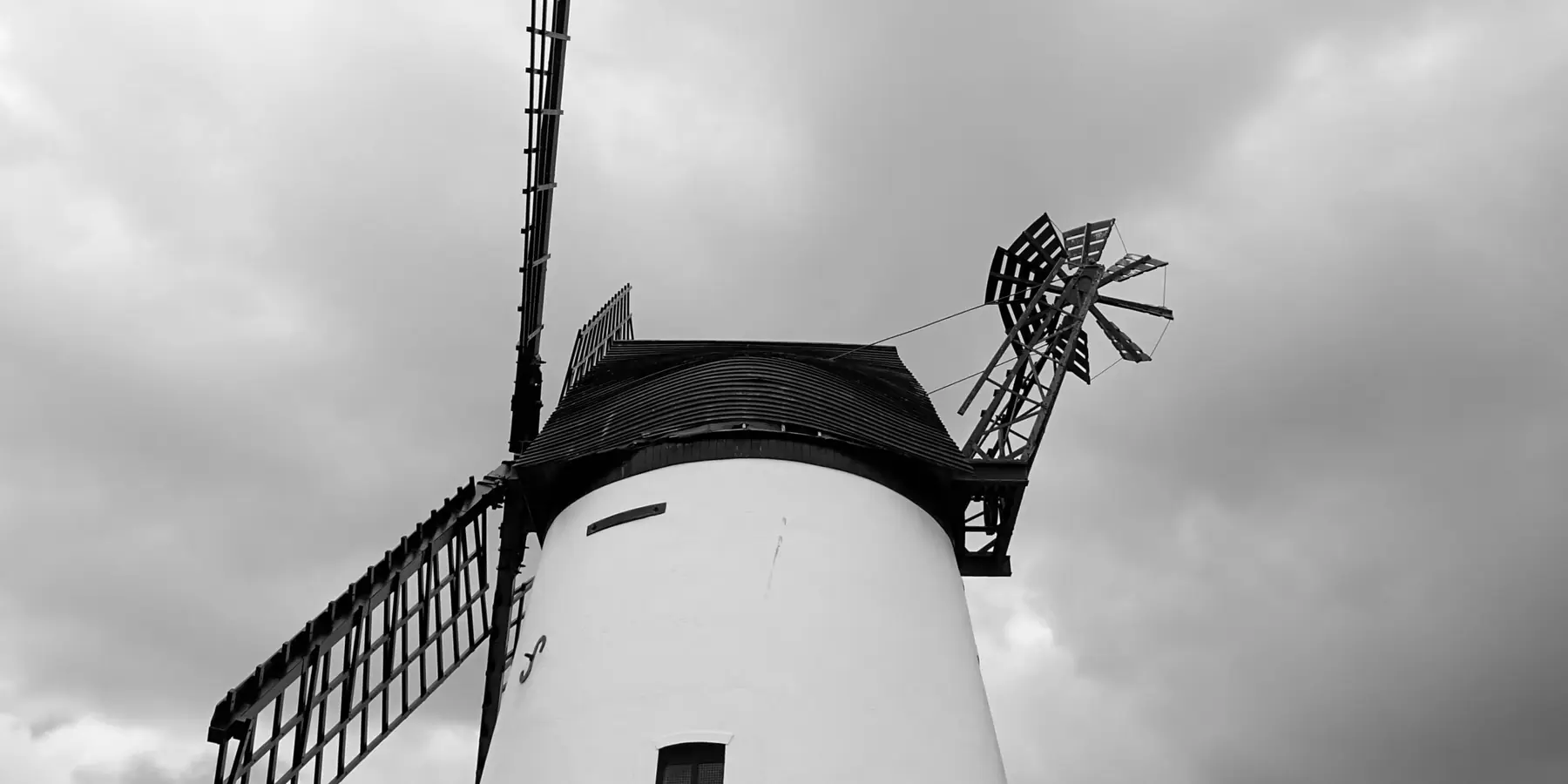 White tower windmill with black cap and sails under a cloudy sky