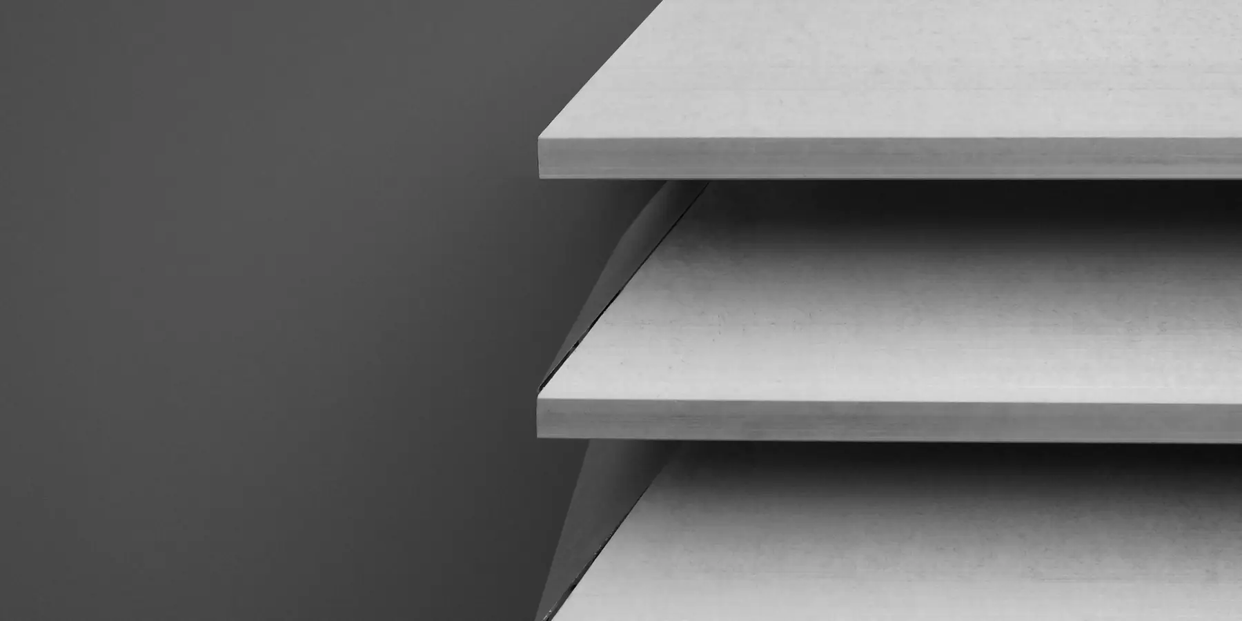 Stacked pale grey shelves in close-up against a dark grey wall