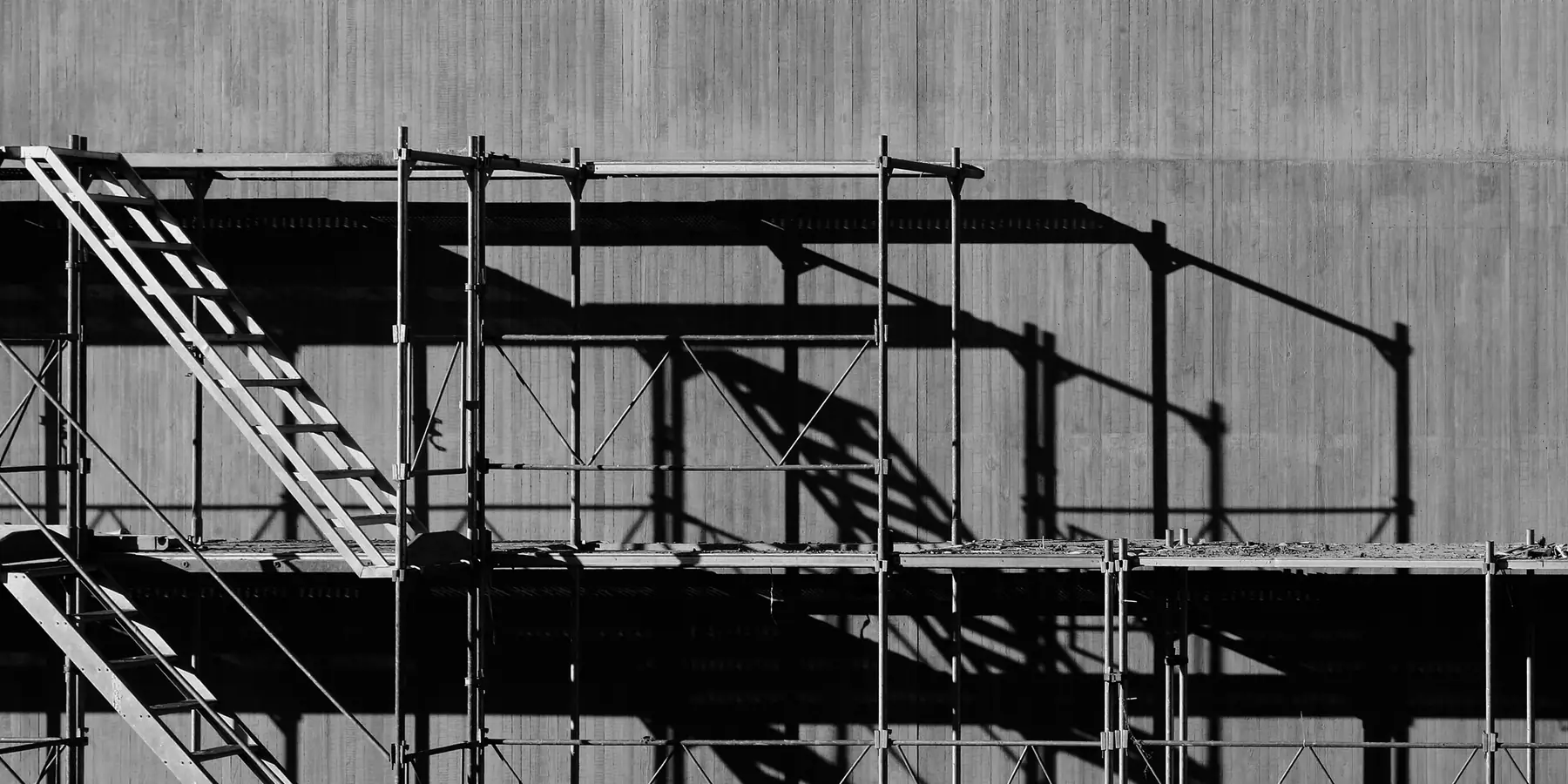 Metal scaffolding with ladders casting long shadows on a concrete wall
