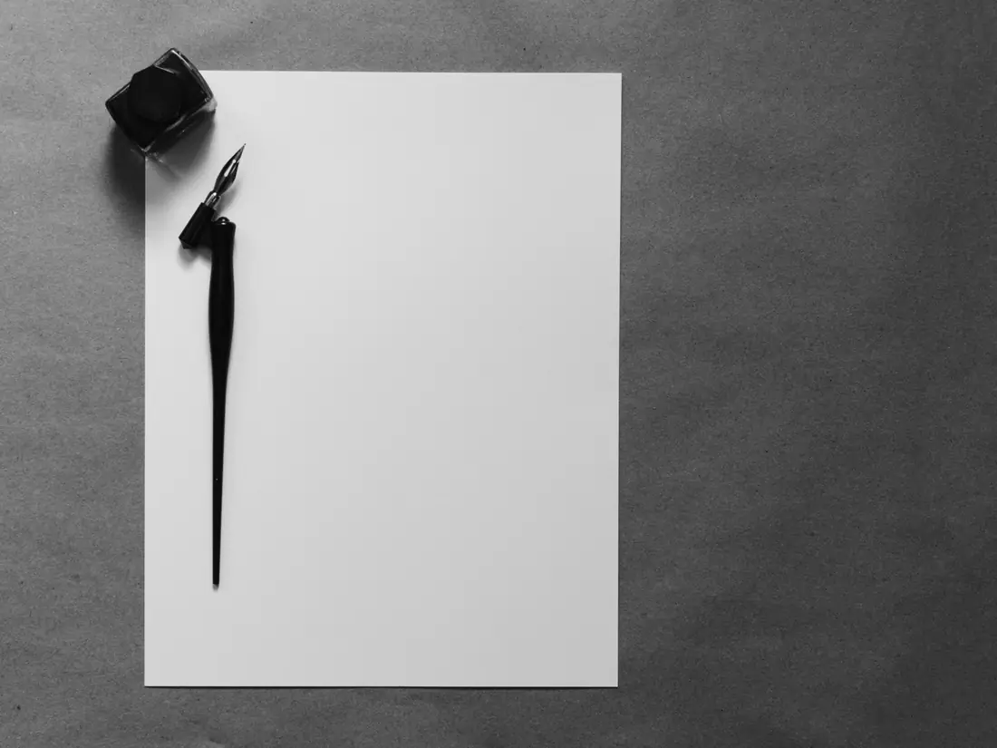 Dip pen and ink bottle beside a blank sheet of paper