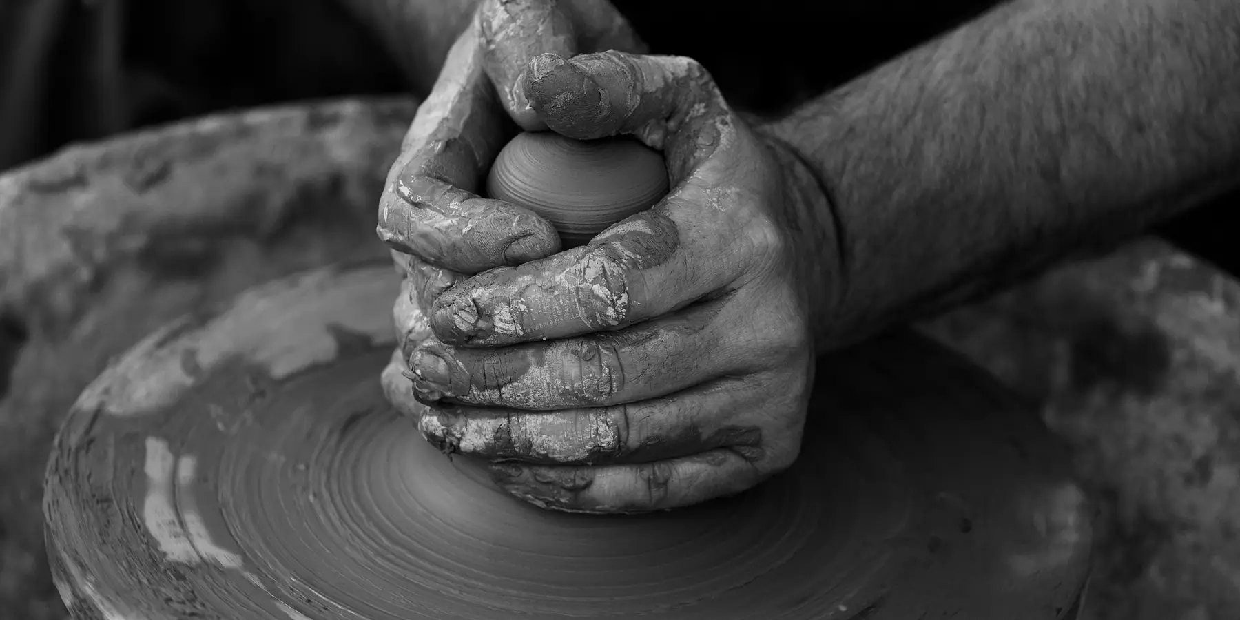 Clay-covered hands shaping a small lump of clay on a spinning pottery wheel