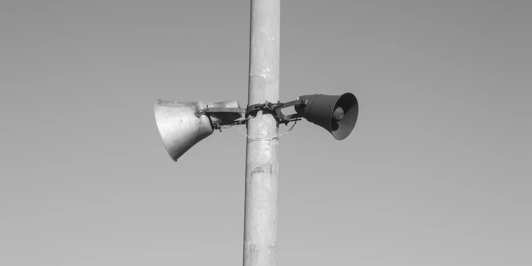Two horn loudspeakers mounted on a pale concrete pole against a clear sky