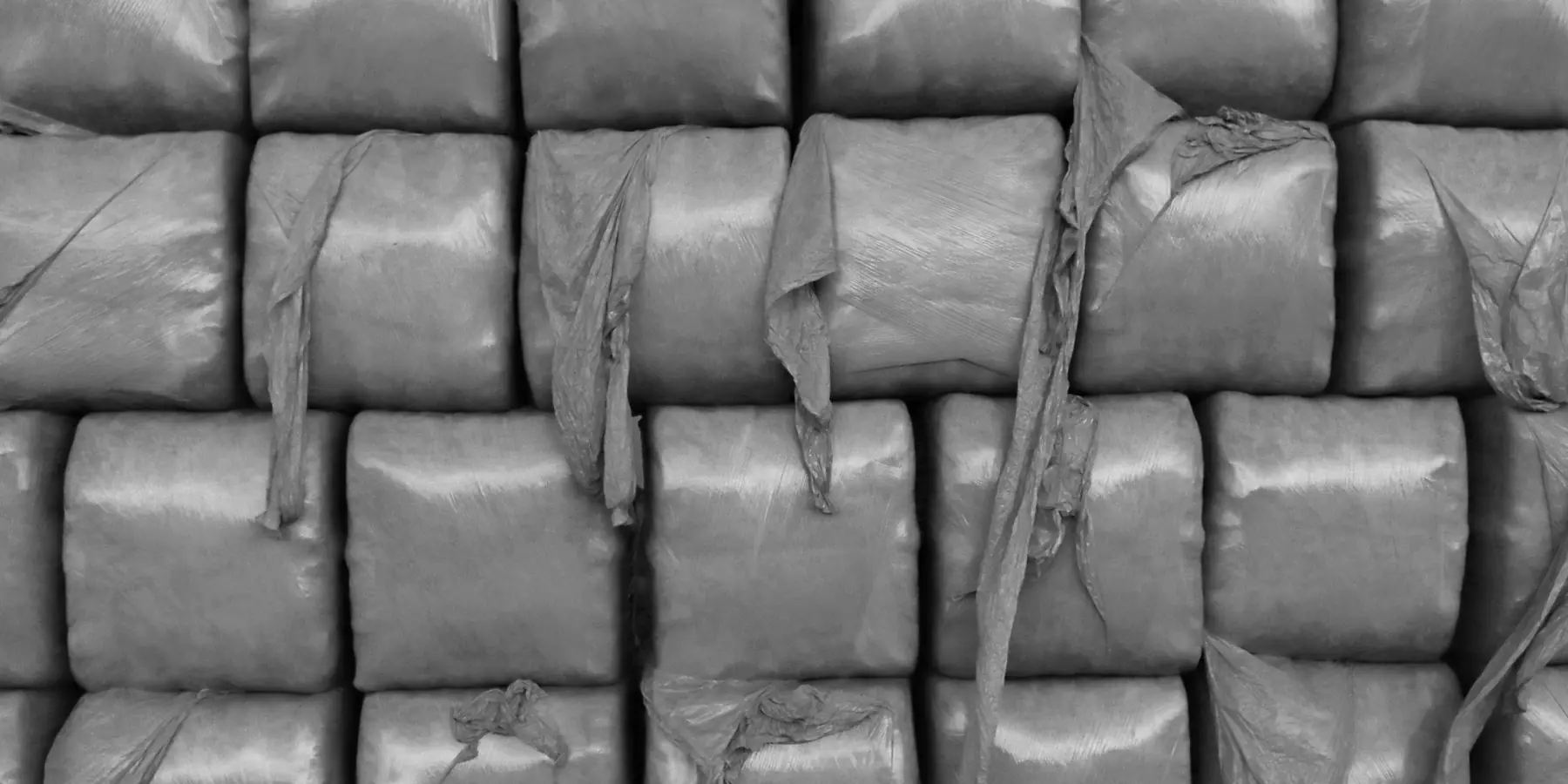 Plastic-wrapped bales stacked in a tight grid, in black and white