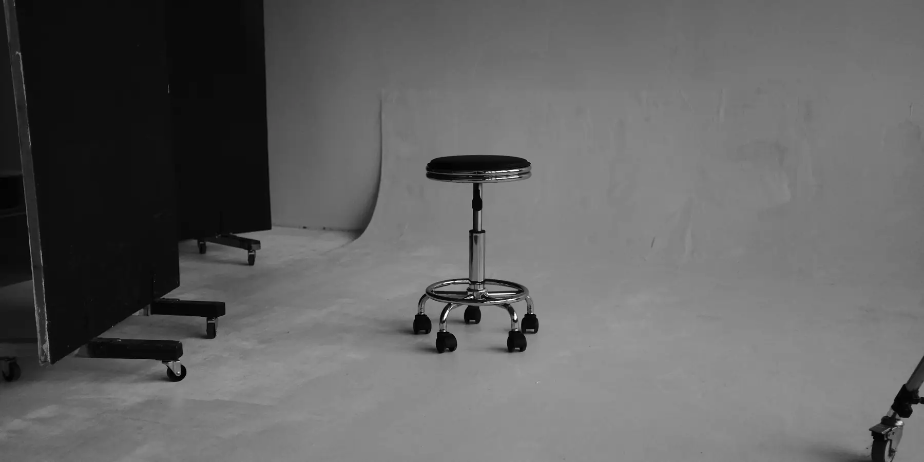 Black swivel stool on casters standing alone in an empty grey room