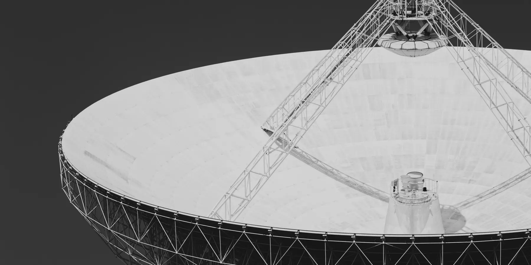 Large white radio telescope dish on a lattice frame against a dark sky
